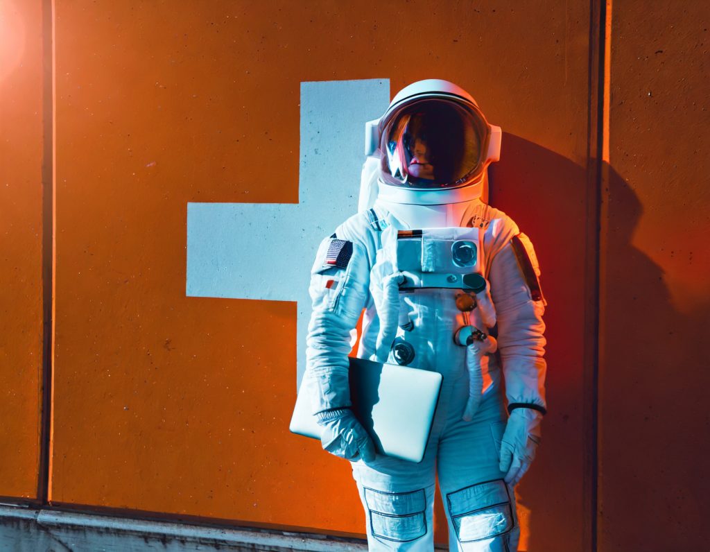 Firefly Astronaut der mit einem Laptop in der Hand vor einer Mauer steht an die Mauer angelehnt is